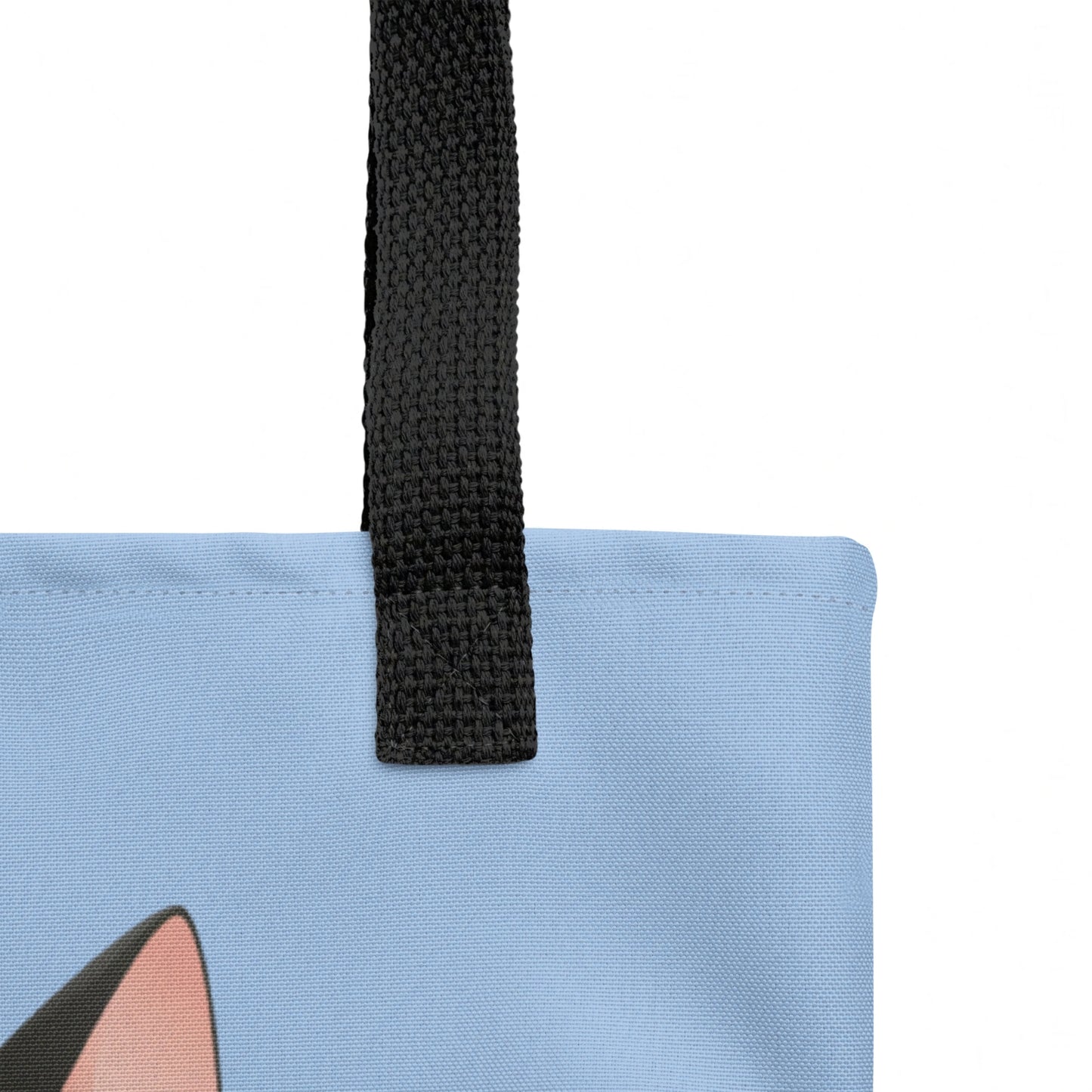 Close-up detail of Freddie tote bag strap join and stitching, cat print visible below against a blue background