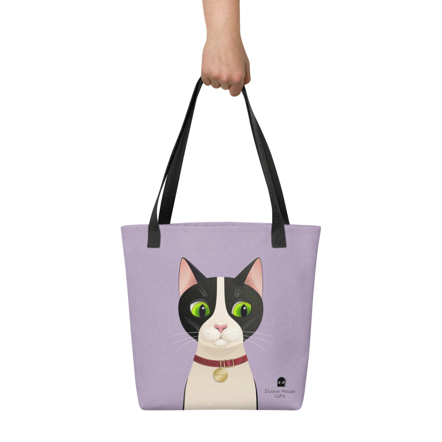 Tote bag with Smudge cat design, shown being held by hand against a lavender backdrop for scale and lifestyle context