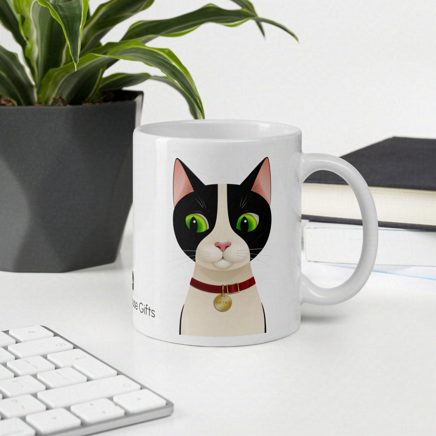 Smudge the tuxedo cat 11oz mug on desk with keyboard and notebooks and plant in the background