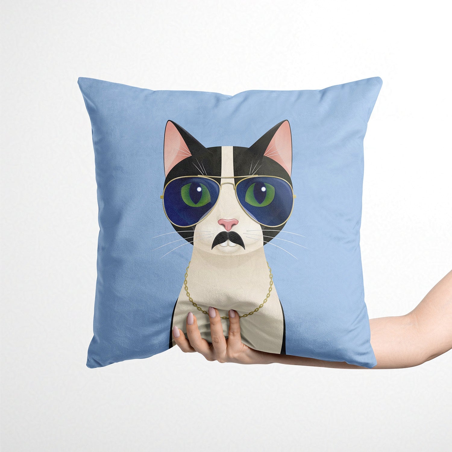 Blue cushion with a cat design wearing sunglasses and a moustache held by a person against a white background.