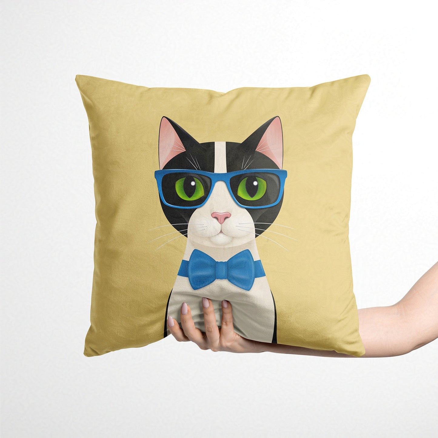 Decorative yellow cushion with a cat design wearing glasses and a bow tie, held by a hand against a white background.